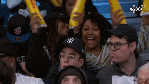 a group of people wearing ny hats are cheering in a crowd