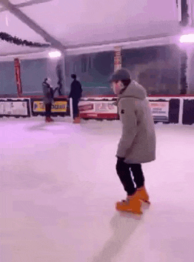a man is ice skating on a rink with a woman standing behind him .