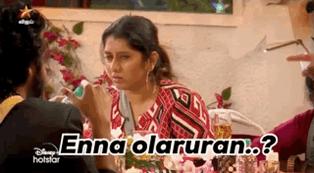 a woman is sitting at a table talking to a man and the words enna olaruran appear on the screen .