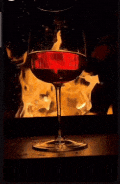 a glass of red wine in front of a fire
