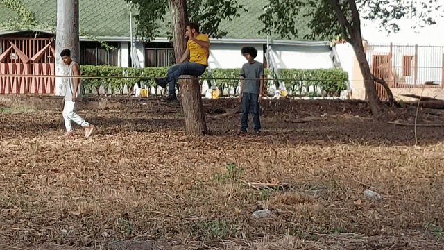 a man in a yellow shirt sits on a tree stump talking on a cell phone