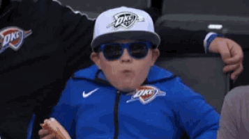a young boy wearing sunglasses and a okc hat