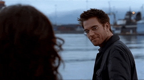 a man wearing glasses and a black jacket looks at a woman