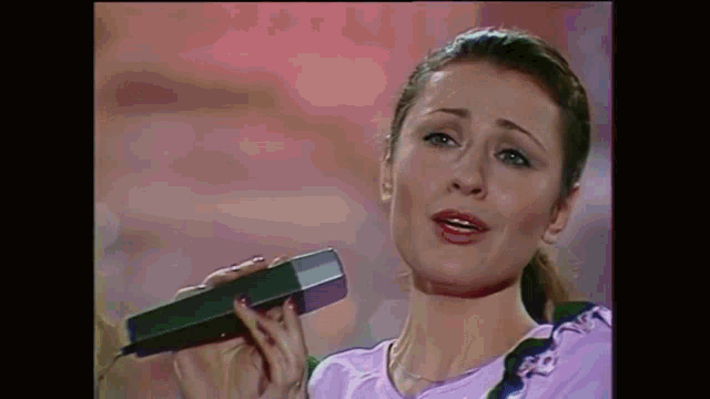 a woman in a purple shirt is singing into a microphone .