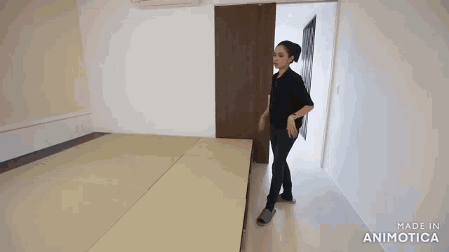 a woman in a black shirt is standing in a room with a sliding door behind her .