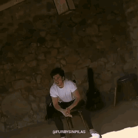 a man wearing a white t-shirt is sitting on a rock and smiling .
