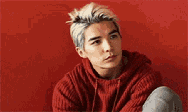a young man in a red sweater is sitting in front of a red wall with his eyes closed .