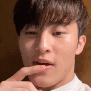 a close up of a young man holding his finger to his mouth .
