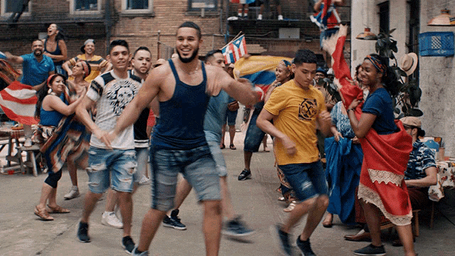a man in a blue tank top is surrounded by a group of people dancing