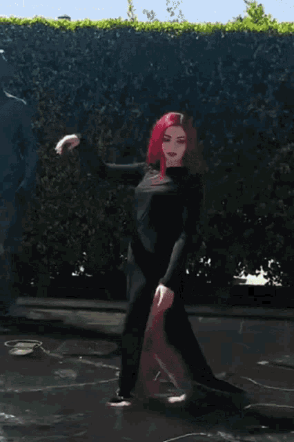 a woman with red hair in a black dress is dancing in a fountain
