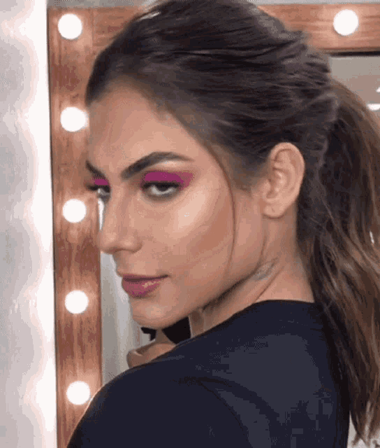 a close up of a woman 's face with a ponytail and pink eyeshadow