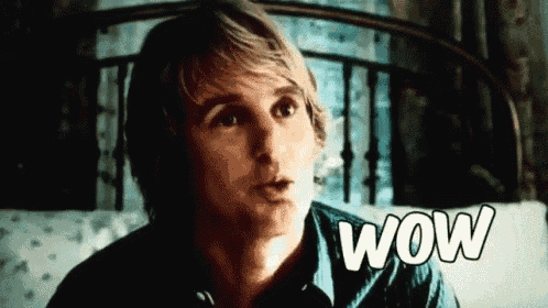 a man is sitting on a bed with the word wow written on the screen .