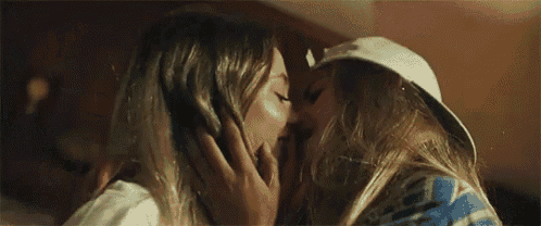 a couple of women are kissing each other in a room . one of the women is wearing a hat .