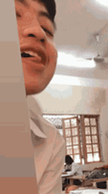 a man in a white shirt is smiling in a classroom with a ceiling fan