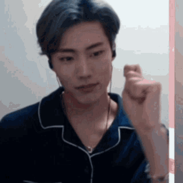 a young man wearing headphones and a blue shirt is making a heart shape with his fist .