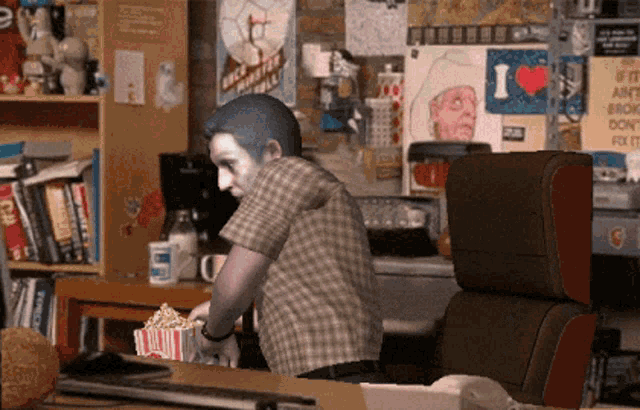a man sitting at a desk with a box of popcorn in front of a poster that says i love you