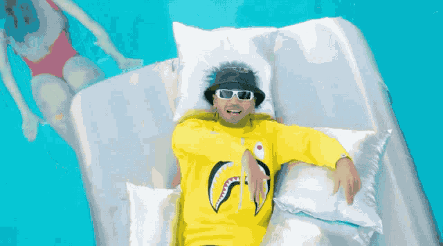 a man wearing a yellow shark shirt is laying on a raft in a pool