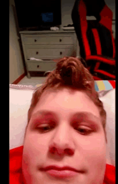 a young man is laying on a bed with a red chair in the background