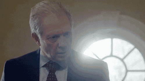 a man in a suit and tie is standing in front of a window with a light shining on his face .