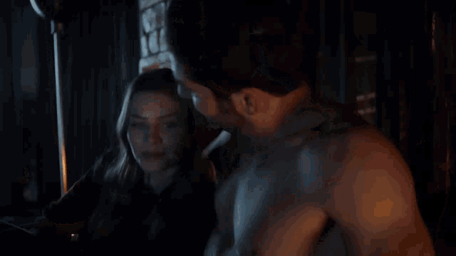 a shirtless man and a woman are hugging in a dark room