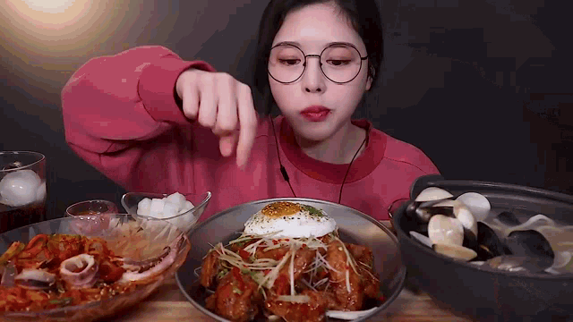 a woman in glasses is eating a plate of food with a fried egg on top