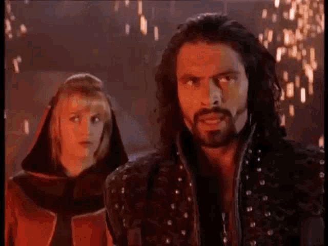 a man with long hair and a beard is standing next to a woman with blonde hair .