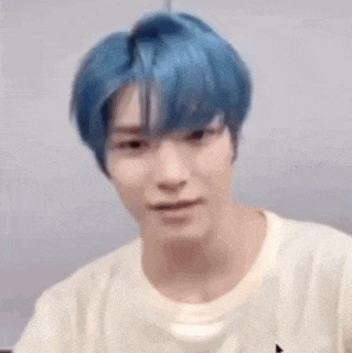 a young man with blue hair and a white shirt is smiling .