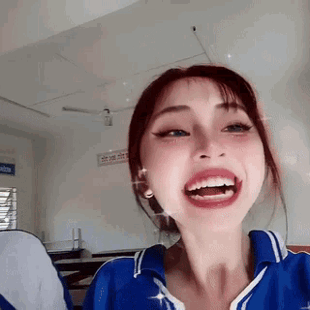 a girl in a blue shirt is laughing with her mouth open .