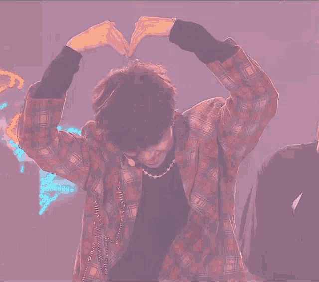 a man in a plaid jacket is making a heart with his hands