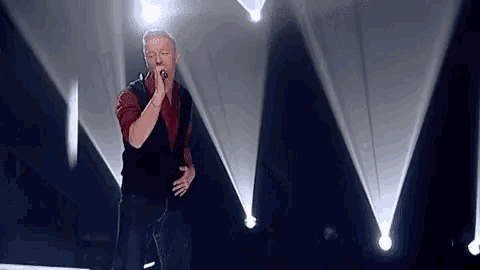 a man is singing into a microphone on a stage in front of a spotlight .