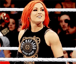 a woman with red hair is standing in a ring wearing a black tank top that says bad ass .