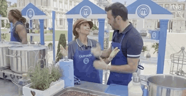 a man and a woman are standing in front of a table with pots and pans .