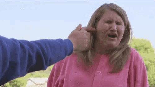 a woman in a pink sweater is being punched in the face by a man in a blue sweater .