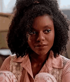 a close up of a woman with curly hair wearing a pink shirt and looking at the camera .