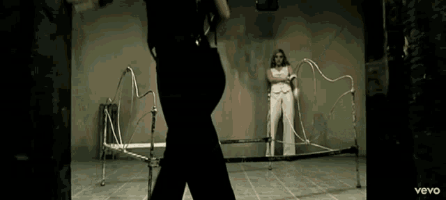 a woman in white pants is standing in front of a bed and a man in black pants is standing behind her