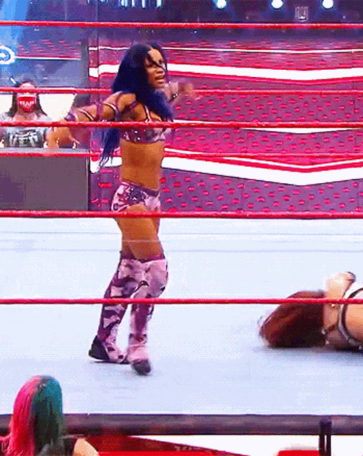 a woman is standing in the middle of a wrestling ring while another woman is laying on the floor .
