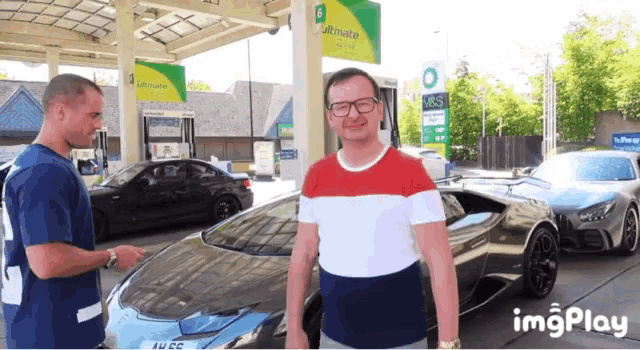 a man in a red white and blue shirt is standing in front of a bp gas station