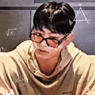 a young man wearing glasses is sitting in front of a chalkboard with mathematical equations written on it .
