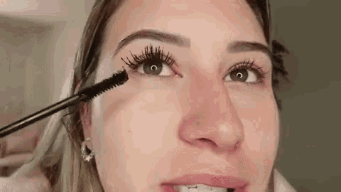 a woman is applying mascara to her eyelashes with a brush .