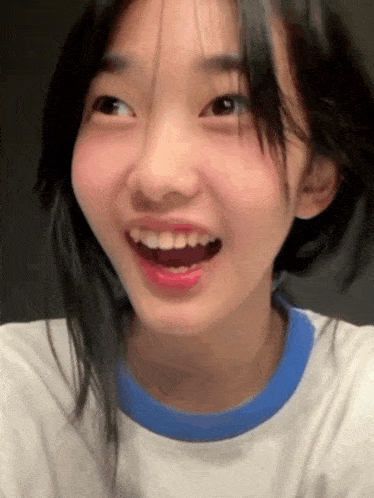 the girl is wearing a white shirt with a blue collar and is smiling with her mouth open .