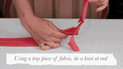 a person is using a tiny piece of fabric to tie a knot at the end .