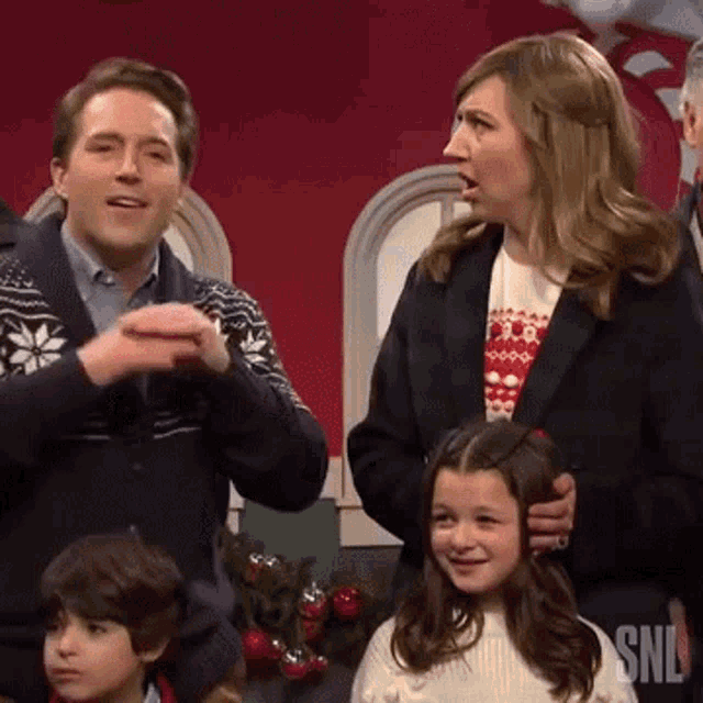 a group of people standing in front of a red wall with the word snl on the bottom