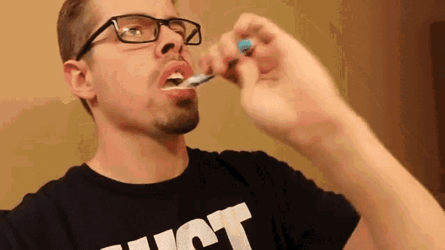 a man wearing glasses is brushing his teeth with a toothbrush while wearing a shirt that says just