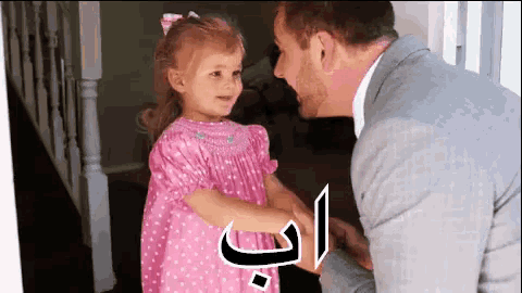 a little girl in a pink dress is shaking hands with a man in a suit ..