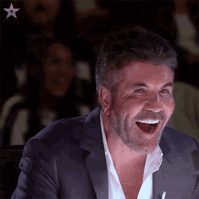 a man in a suit and white shirt is laughing with his mouth wide open