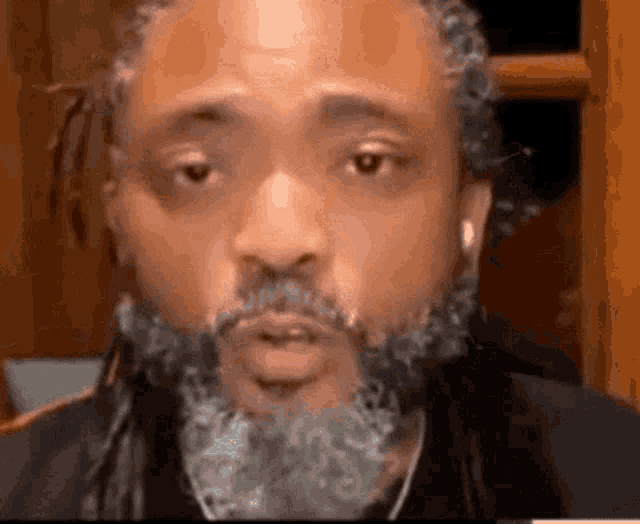 a man with a beard and dreadlocks is wearing headphones and looking at the camera .