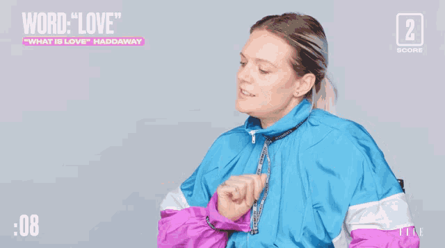 a woman in a blue and purple jacket is dancing in front of a sign that says " word love "