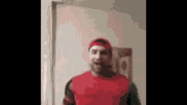 a man in a red shirt and red hat is standing in front of a door .