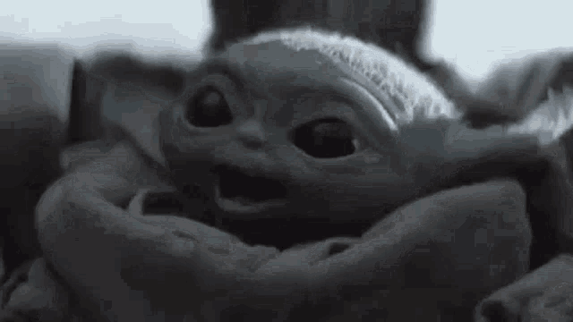 a baby yoda from the mandalorian is sitting in a blanket and smiling .