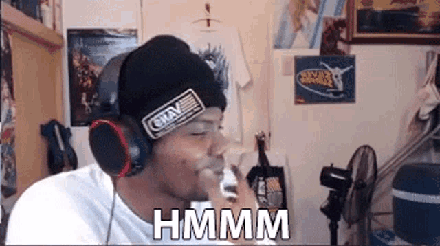 a man wearing headphones and a beanie is smoking a cigarette and says hmmm .